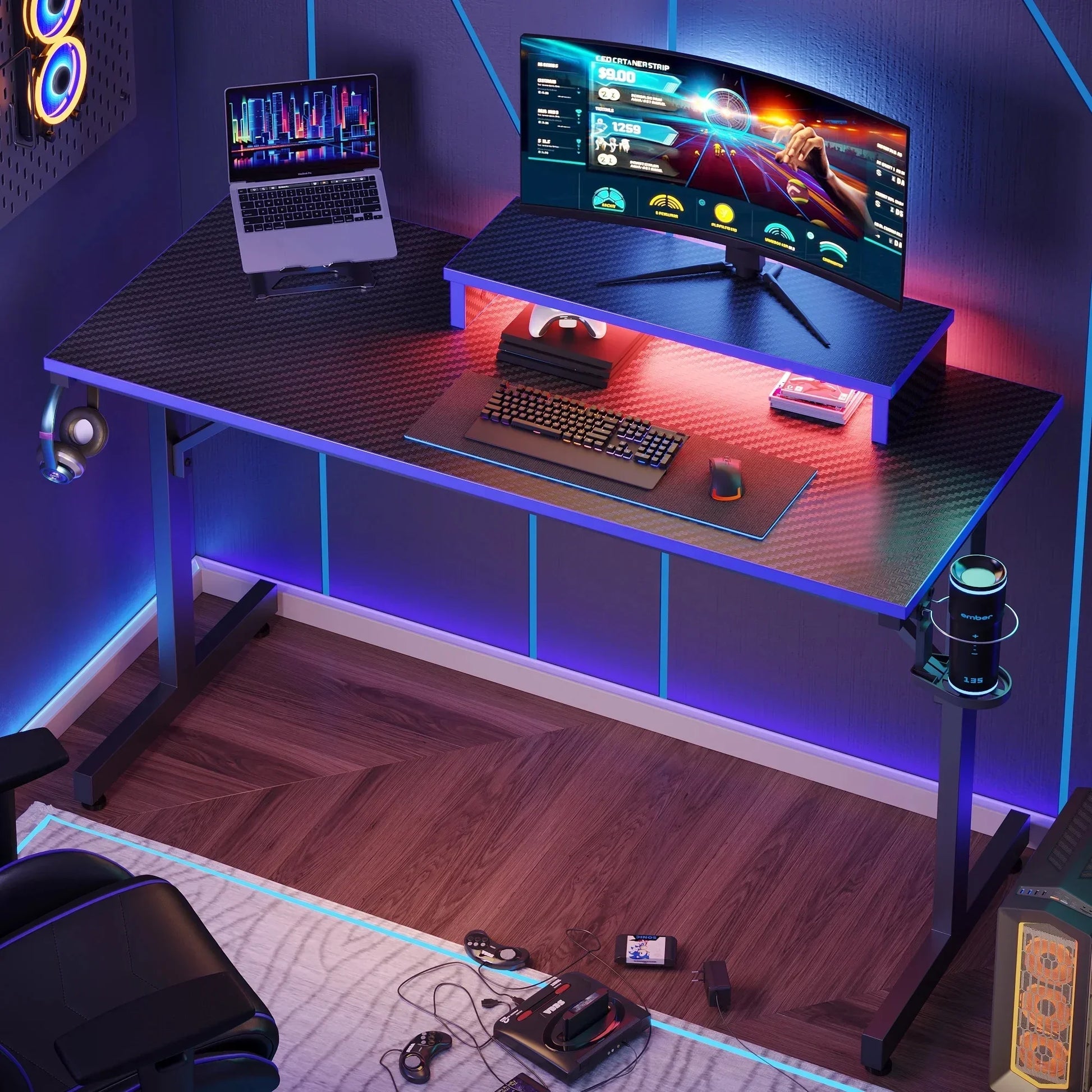 Modern gaming desk setup with curved widescreen monitor, laptop, RGB lighting, keyboard, mouse, headphones, and retro console