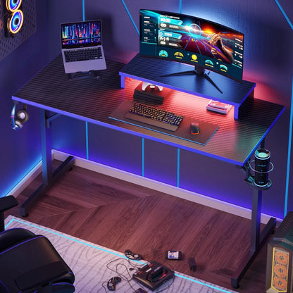 Modern gaming desk setup with curved widescreen monitor, laptop, RGB lighting, keyboard, mouse, headphones, and retro console