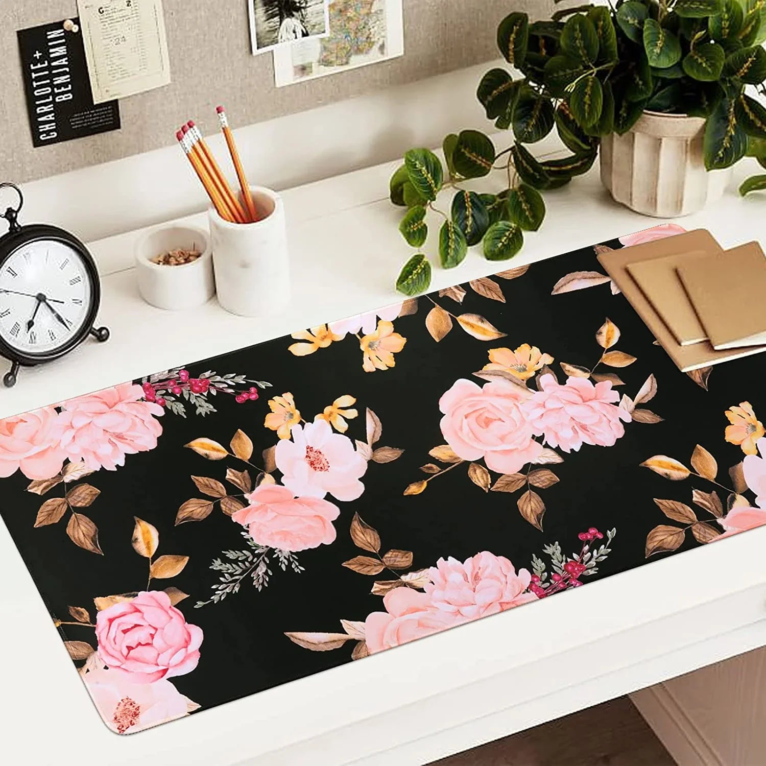 Floral desk mat with pink and peach flowers on black background, decorated workspace with pencils, clock, plant