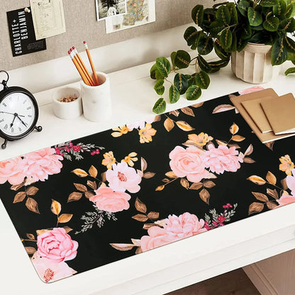 Floral desk mat with pink and peach flowers on black background, decorated workspace with pencils, clock, plant