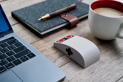 Retro 8-bit gaming mouse next to laptop, notebook, and coffee on wooden desk