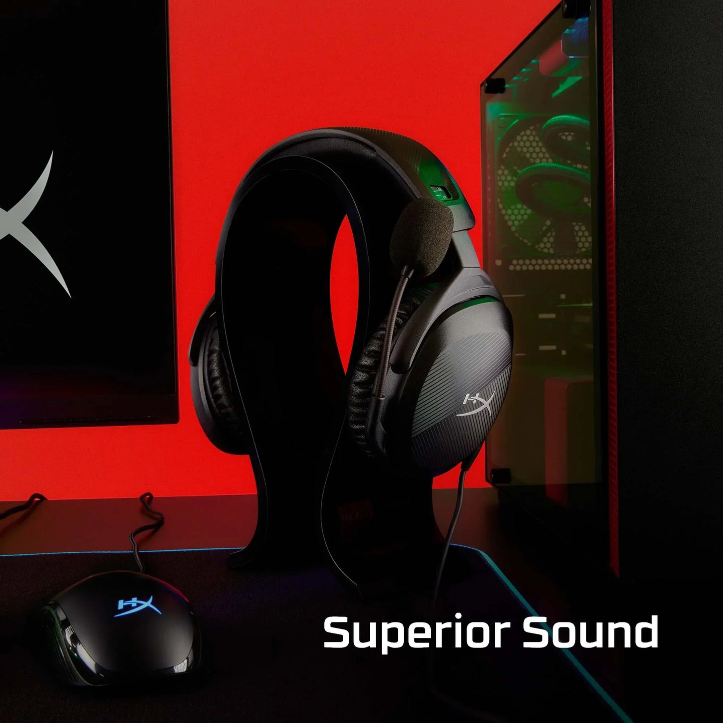 HyperX gaming headset with microphone on stand next to gaming mouse and PC tower with red background