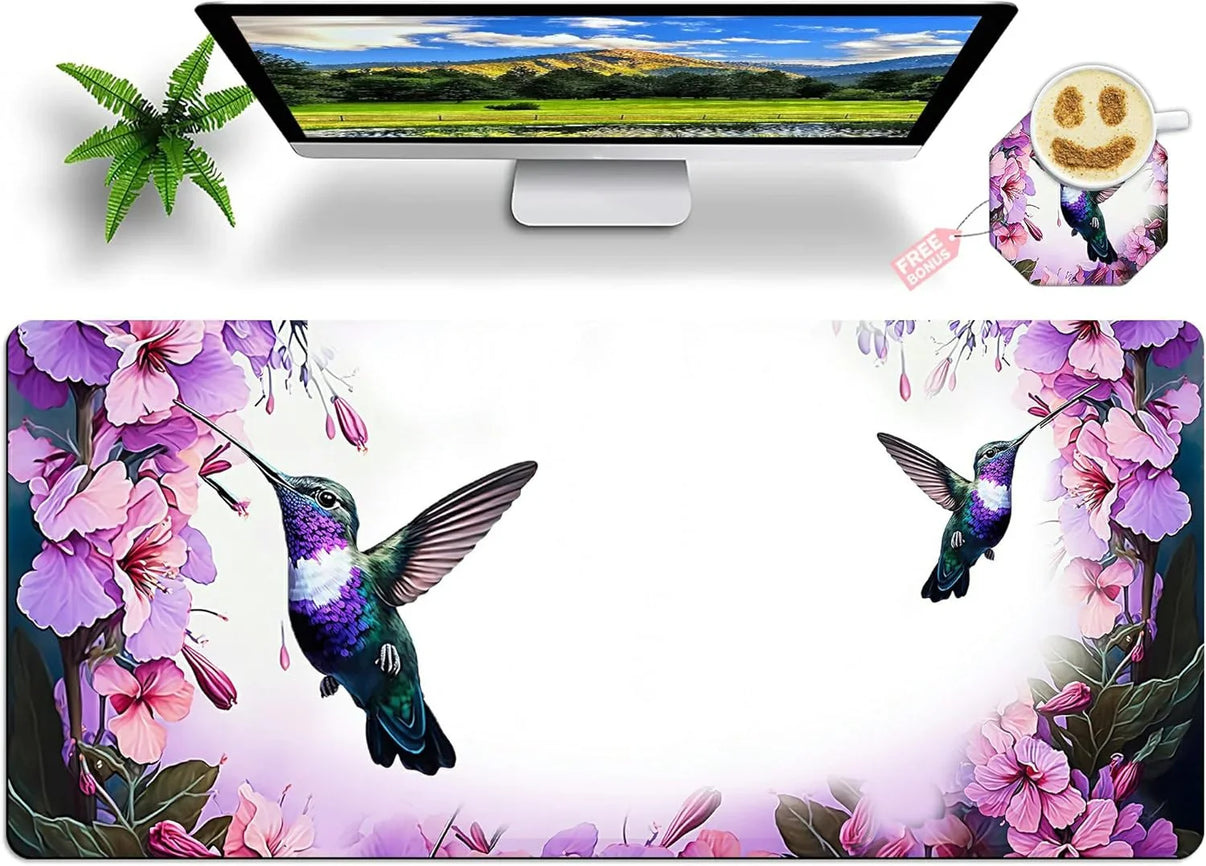 Desk setup with computer, green plant, hummingbird-themed mouse pad and matching cup coaster with smiley coffee art