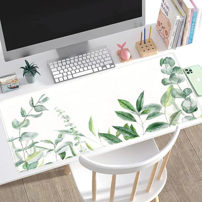 Minimalist white workspace with computer, keyboard, green leafy desk mat, and decorative items