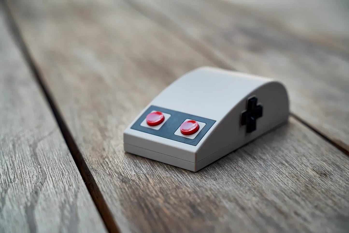 Retro 8-bit style gaming mouse with red buttons and D-pad on wooden surface