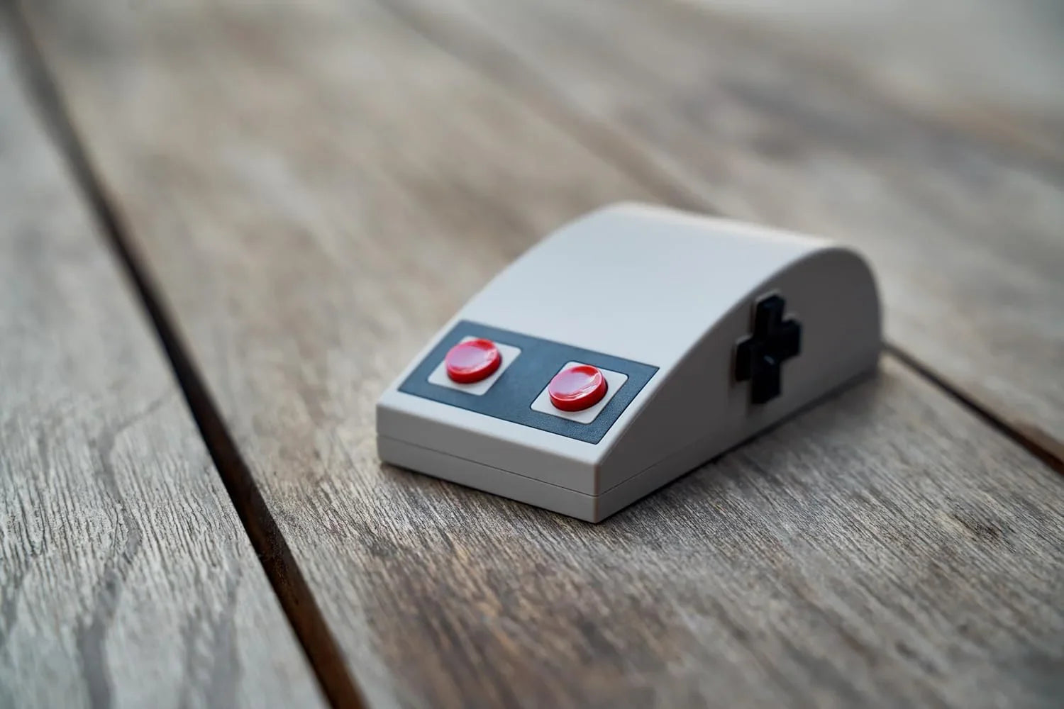 Retro 8-bit style gaming mouse with red buttons and D-pad on wooden surface