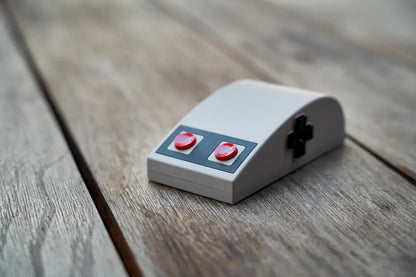 Retro 8-bit style gaming mouse with red buttons and D-pad on wooden surface