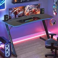 Modern gaming setup with dual monitors showing fantasy game art, RGB keyboard, speakers, gaming chair, and LED lights
