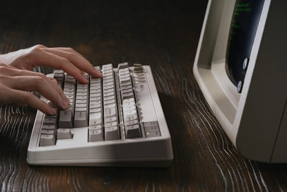 Hands typing on retro mechanical keyboard beside vintage computer monitor on wood desk