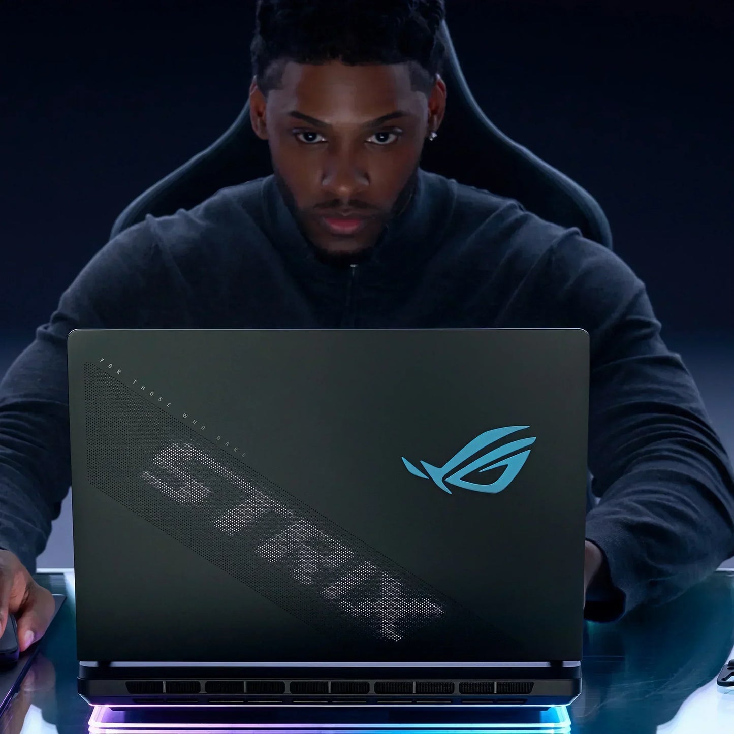 Gamer using ASUS ROG Strix gaming laptop at a desk with RGB lighting