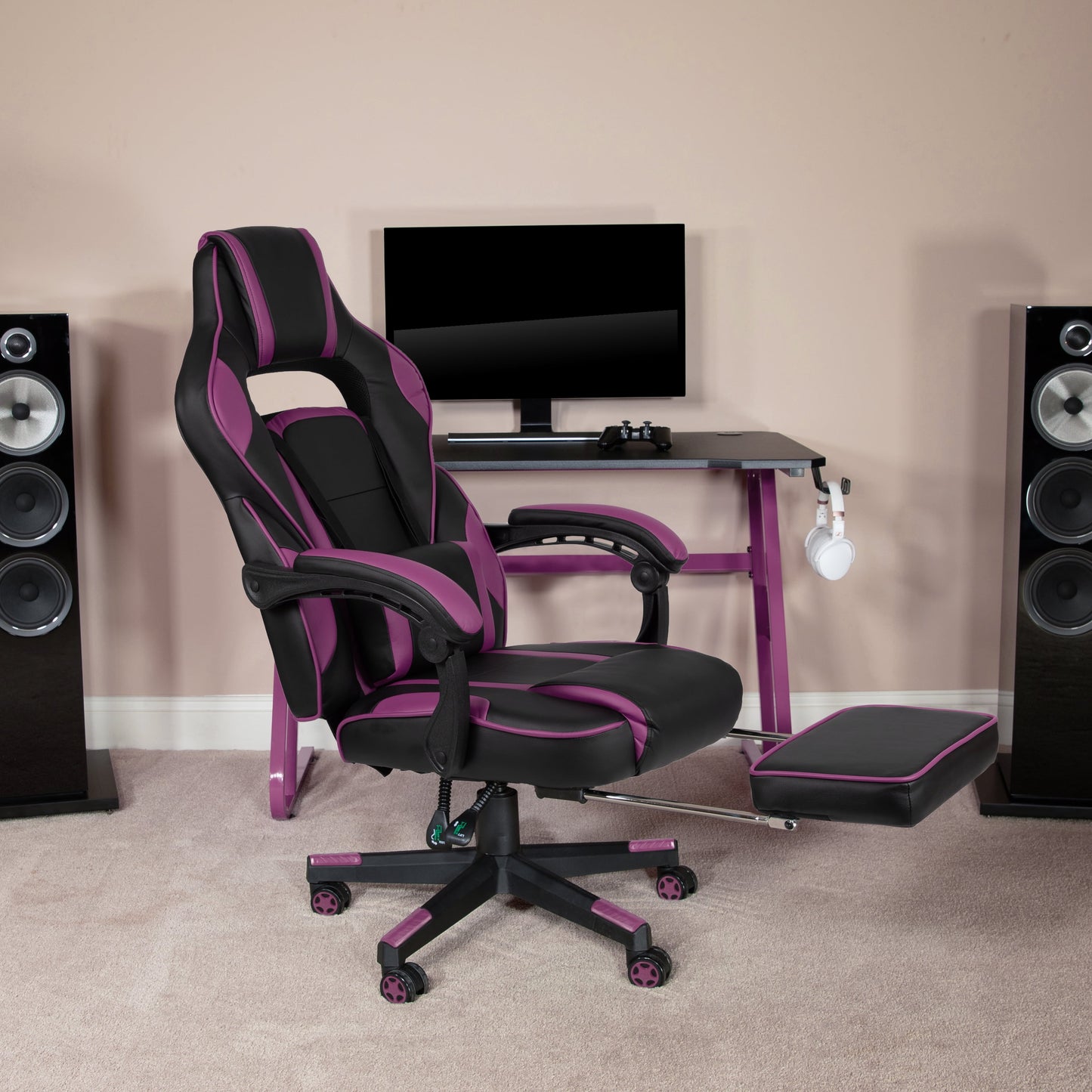 Purple and black gaming chair with footrest, desk, monitor, and speakers setup