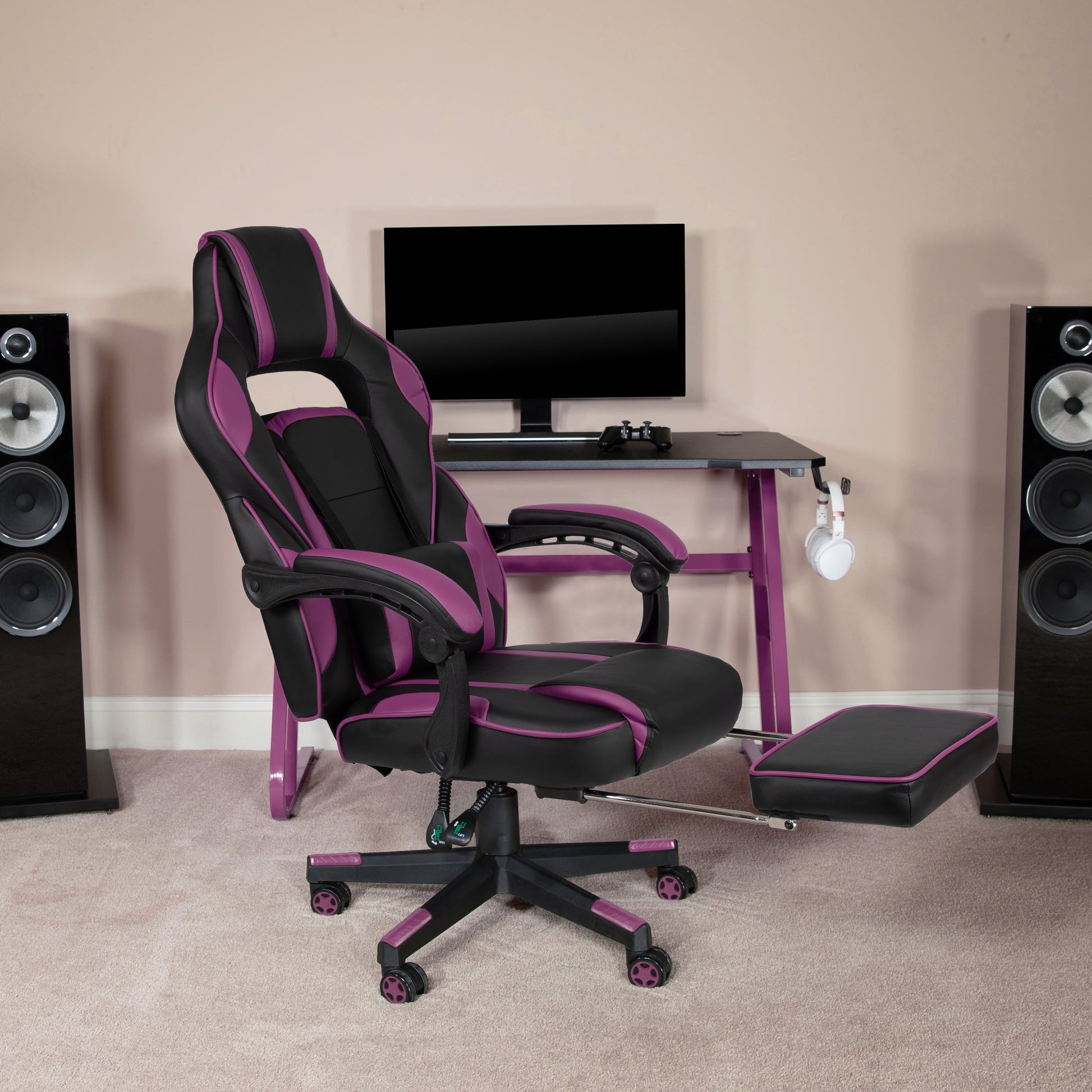 Purple and black gaming chair with footrest, desk, monitor, and speakers setup