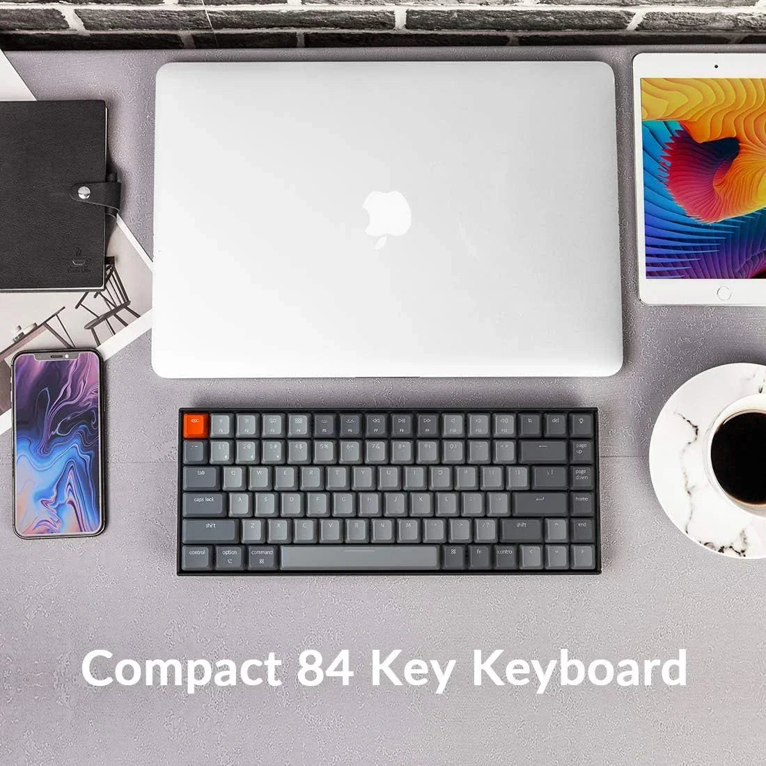 Compact 84 key retro keyboard with laptop, tablet, phone, and coffee on modern desktop