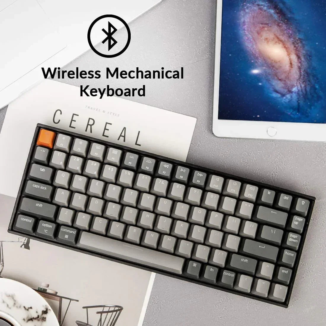 Wireless mechanical keyboard with gray keys next to a tablet and magazine, modern gaming setup.
