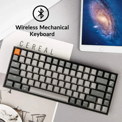 Wireless mechanical keyboard with gray keys next to a tablet and magazine, modern gaming setup.