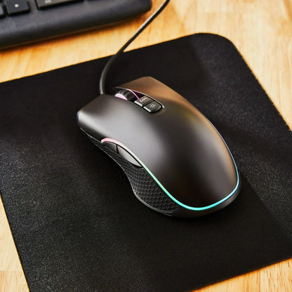 RGB gaming mouse with side buttons on mouse pad, wooden desk, and keyboard corner