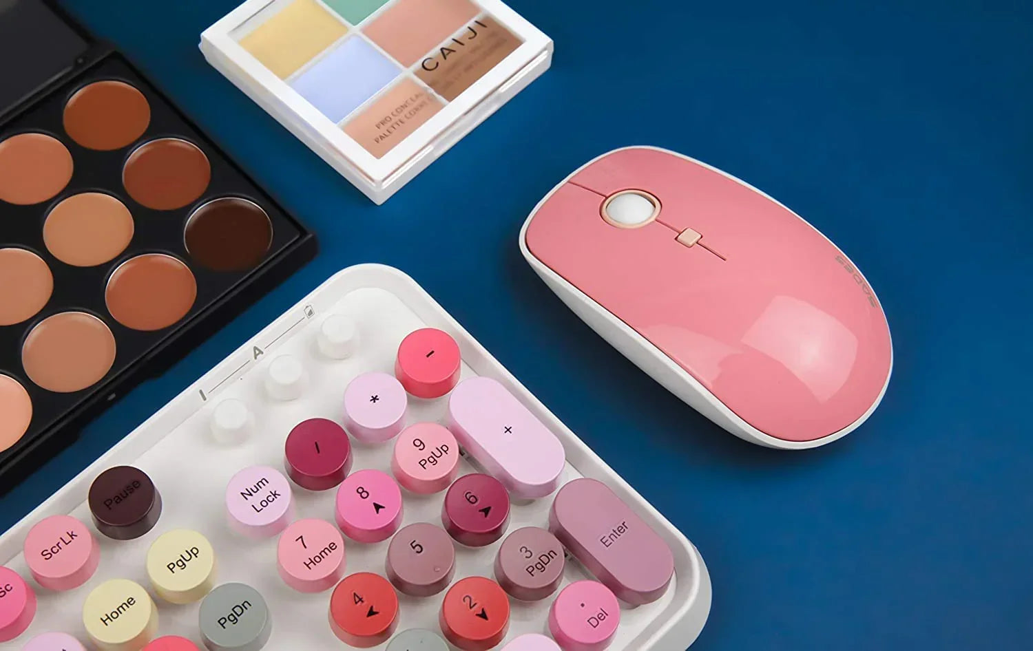 Pink wireless mouse and pastel retro-style mechanical keyboard with makeup palettes on blue background