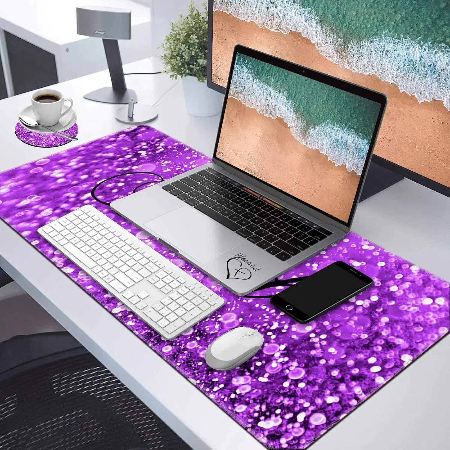 Modern workspace with laptop, white keyboard, mouse on purple bubbly desk mat, smartphone, coffee cup, and monitor