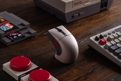 Retro-inspired gaming mouse with red buttons, vintage console, cartridges, and keyboard on wood desk