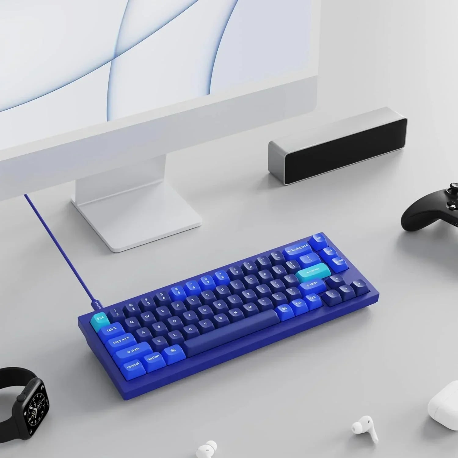 Retro blue gaming keyboard on a modern desk with monitor, headphones, watch, and controller