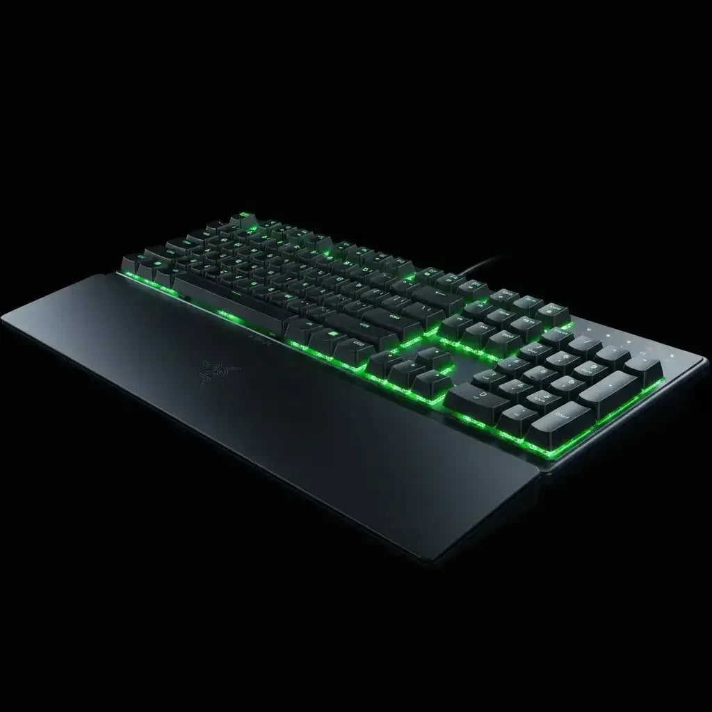 Mechanical gaming keyboard with green LED backlighting and attached black wrist rest on black background
