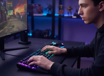 Young man focused gaming at desk with RGB mechanical keyboard and colorful game on monitor