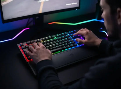 Person using RGB backlit gaming keyboard with rainbow lighting and wrist rest in dark gaming setup