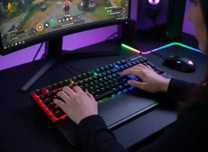 Person using RGB backlit mechanical gaming keyboard and mouse with curved monitor gaming setup
