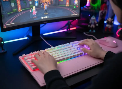 Gamer using pink RGB mechanical keyboard and mouse at colorful gaming setup with monitor