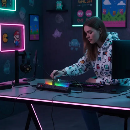 Young woman in gaming hoodie connecting cable to RGB power strip in neon-lit gaming room