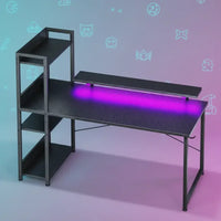 Modern gaming desk with carbon fiber finish, purple LED light, and side shelves against blue-pink background with retro gaming icons.