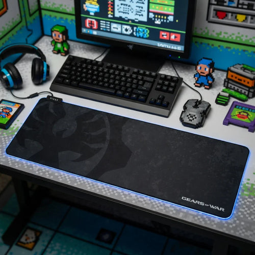 Retro gaming desk setup with RGB Gears of War mouse pad, pixel art mouse, keyboard, and headset.
