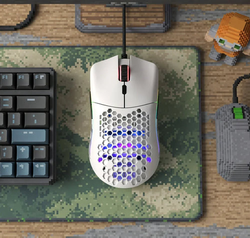 White honeycomb gaming mouse with RGB lights on pixel art mousepad, next to keyboard